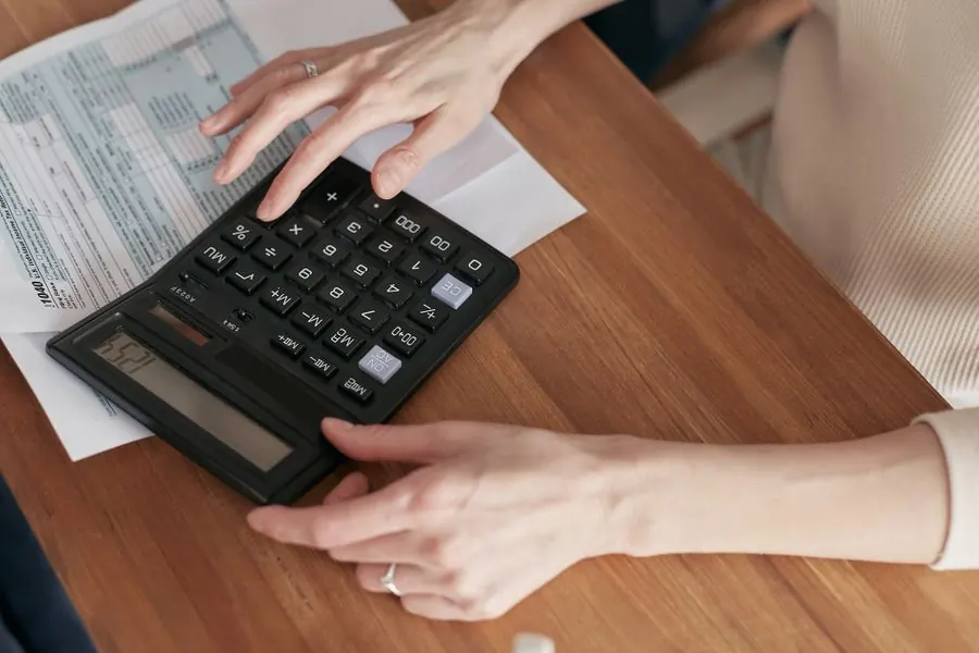 Pessoa fazendo contas com calculadora e contas da casa